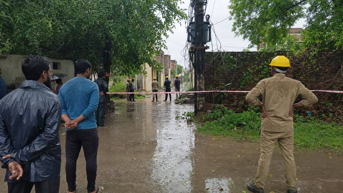 Electricity department staff inspecting a power pole in Varanasi during monsoon season