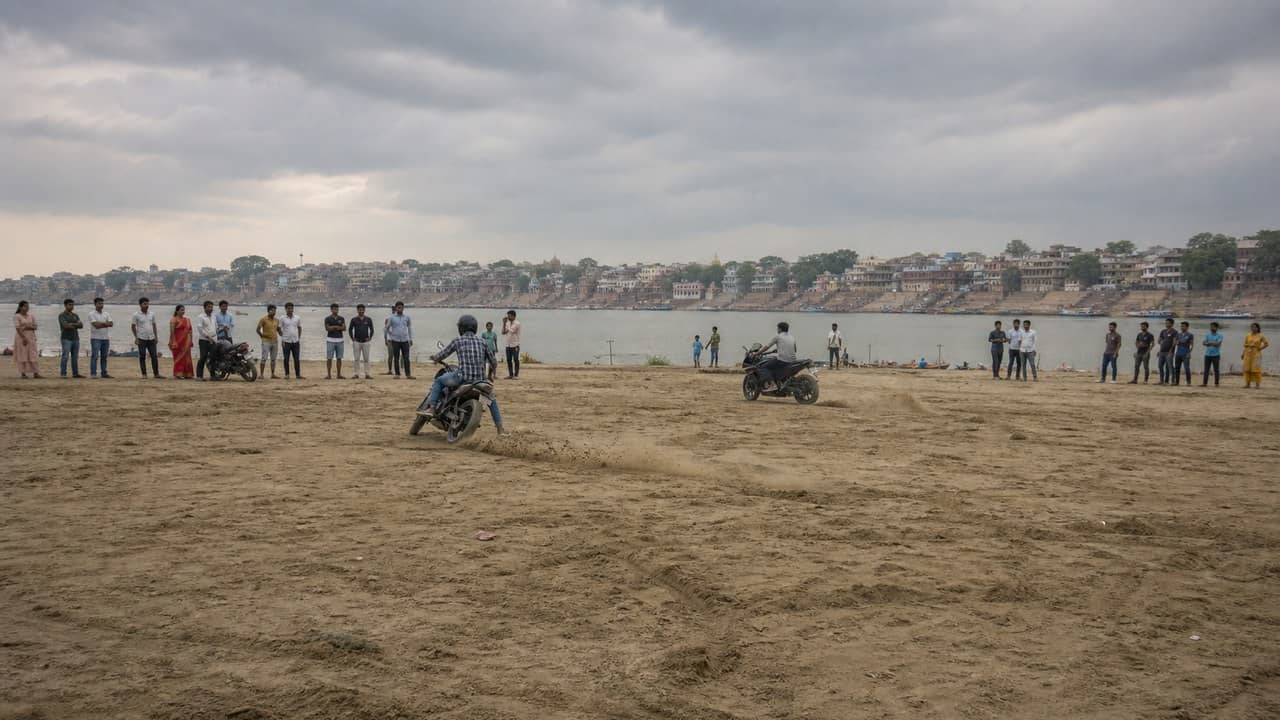 Motorcycles seen at a distance on Ganga sandbanks near Varanasi with residents watching