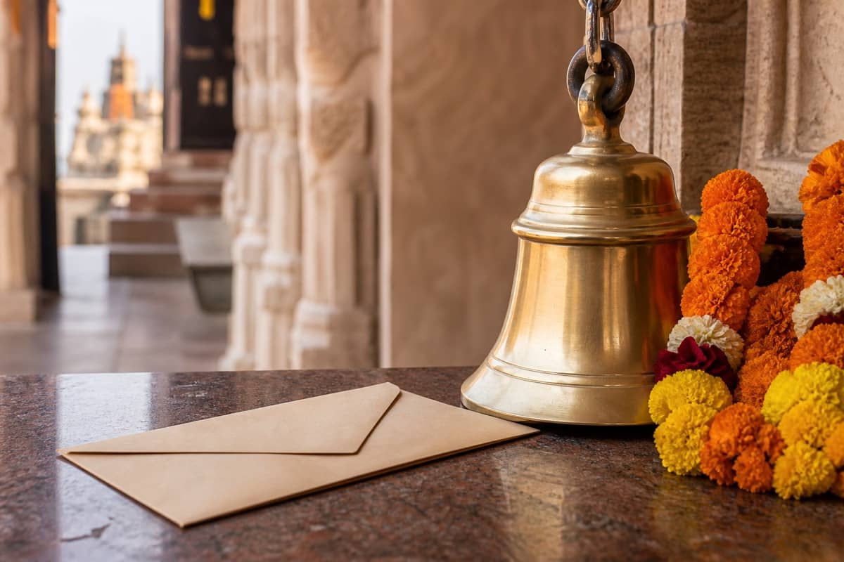Brass temple bell, marigold garlands and a sealed donation envelope in a sandstone corridor