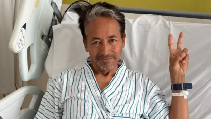 A recovering activist outside a modern hospital with supporters standing at a respectful distance