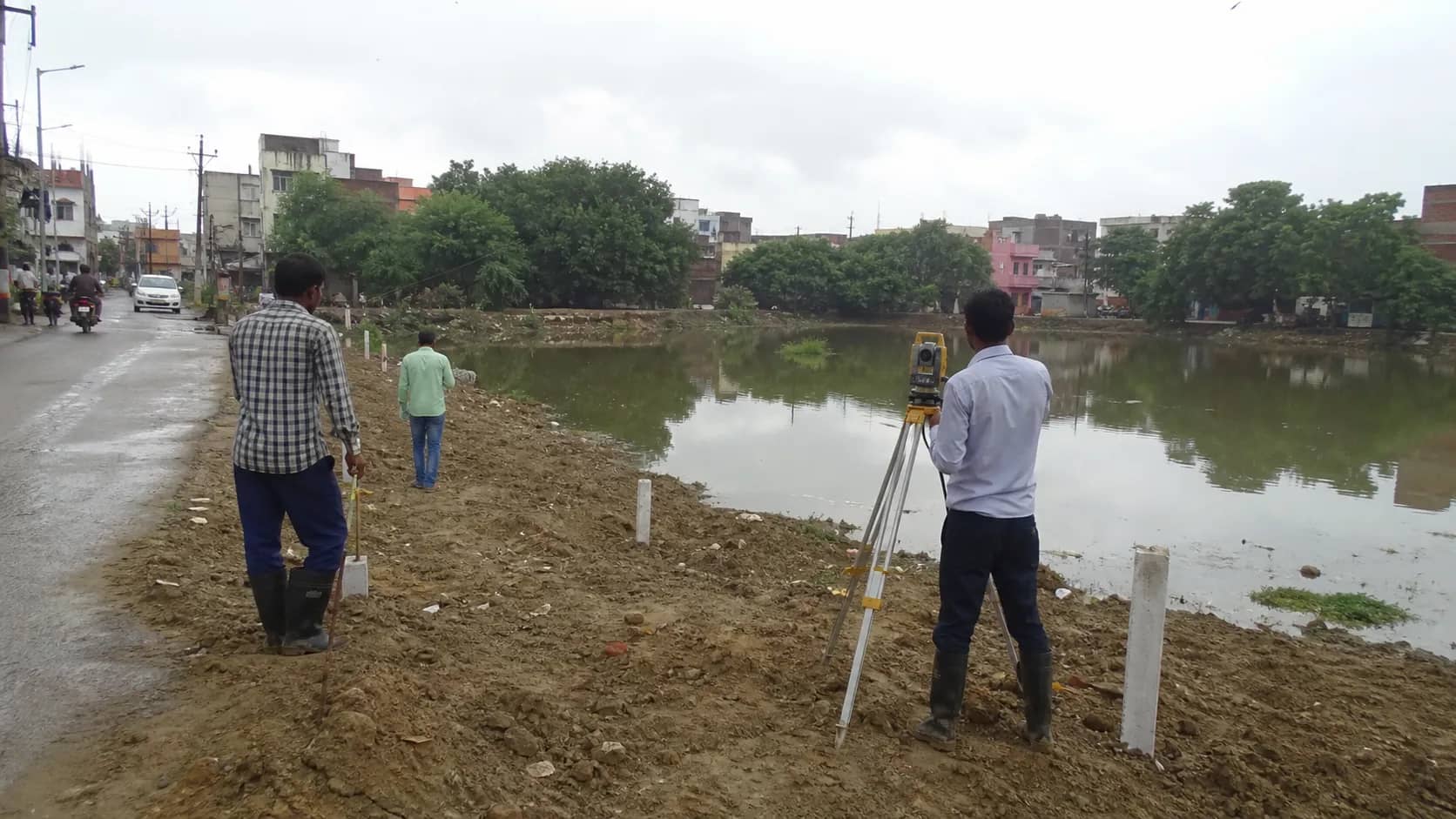Municipal survey and earthwork underway beside a reclaimed urban pond site in Kakarmatta, Varanasi