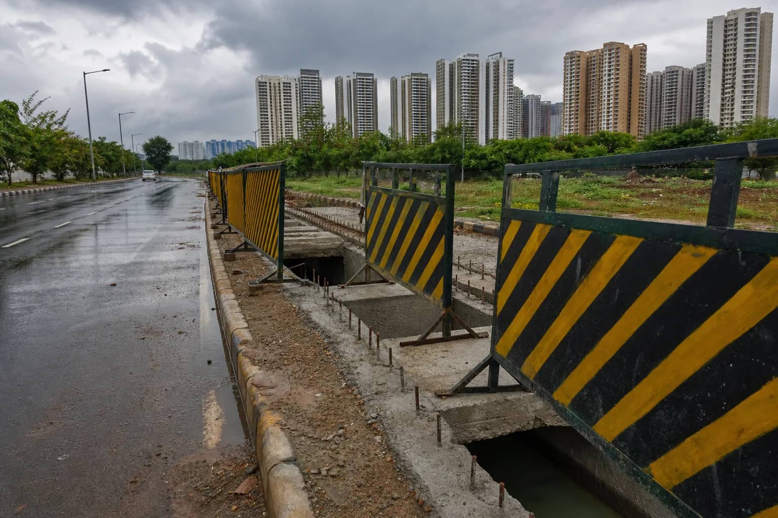 Barricaded storm drain construction beside a wet Sector 70A road in Gurugram
