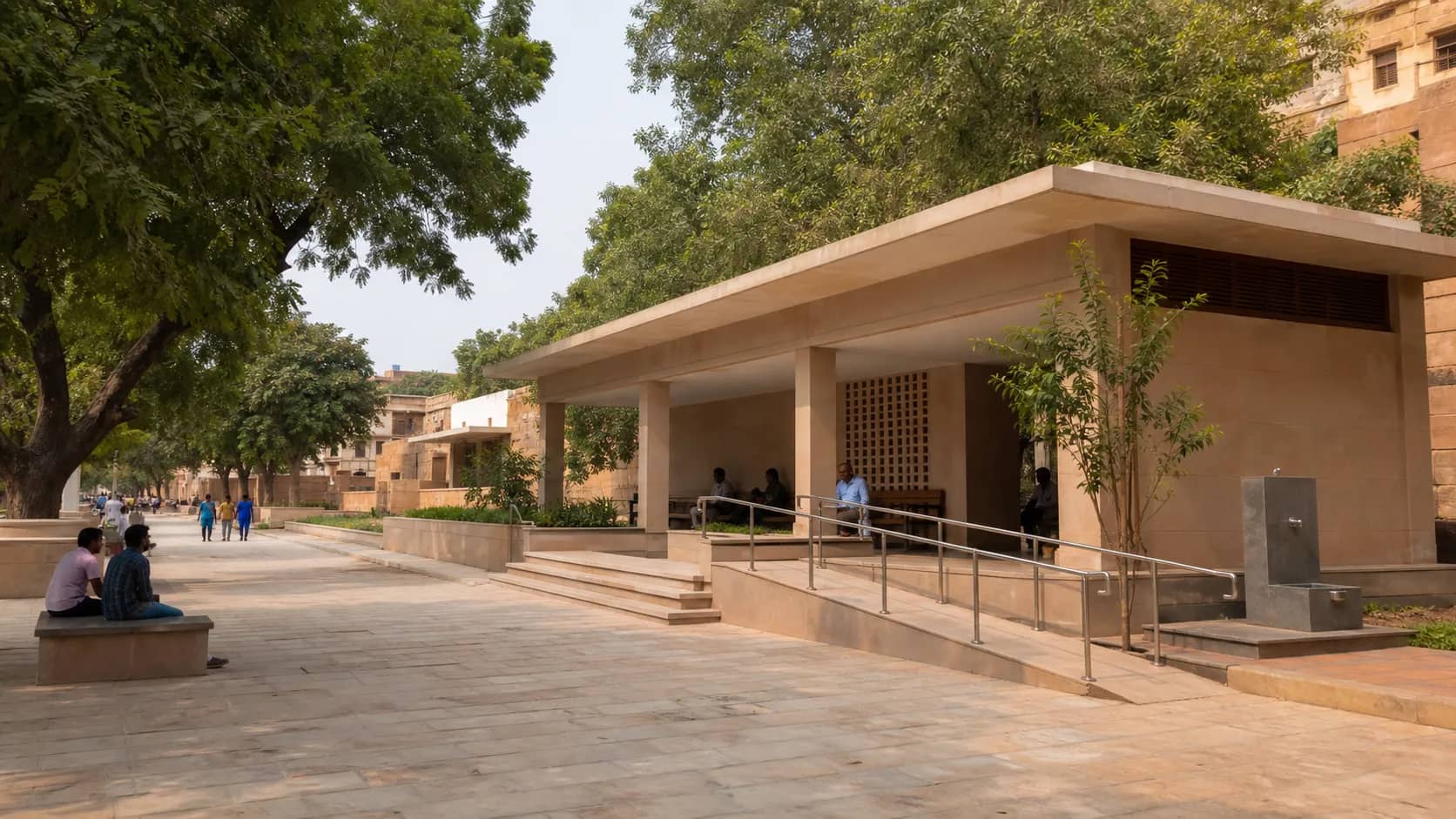 A modest visitor facility building beside a heritage walkway in Varanasi with shaded seating