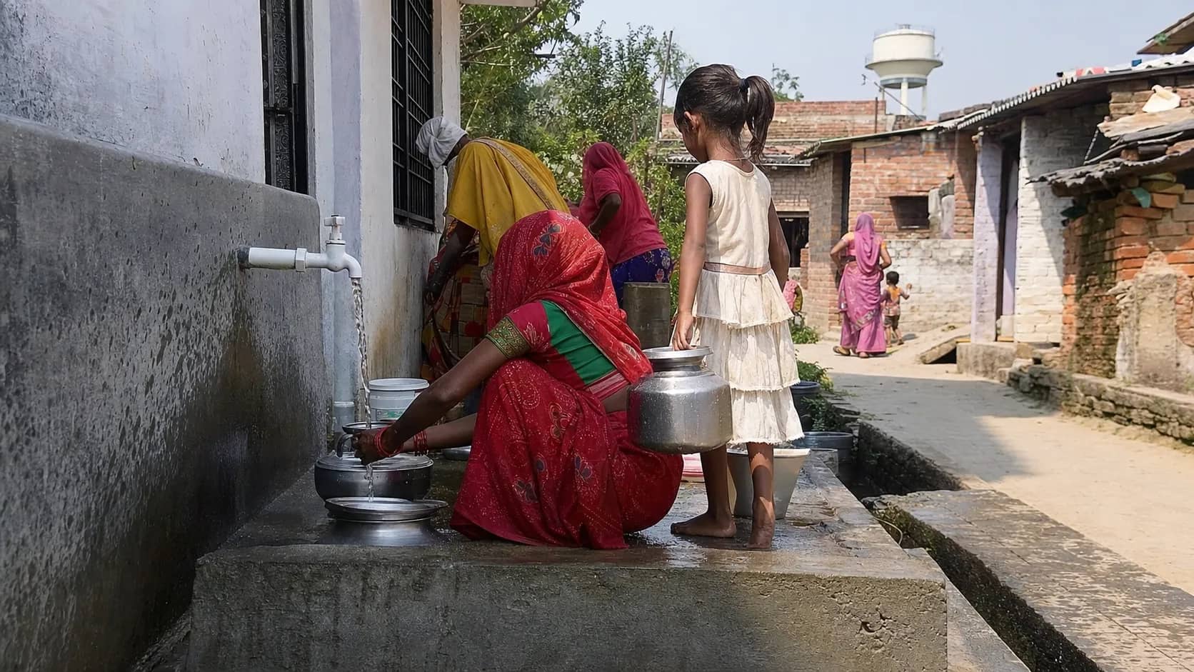 Women filling metal containers from a new piped drinking water tap in a Varanasi village
