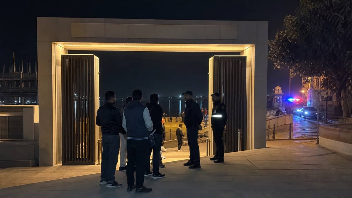 Visitors and security staff speaking near a riverside ghat entrance at night