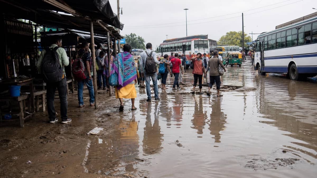 Commuters navigating puddles and mud at a rural bus stop near Varanasi