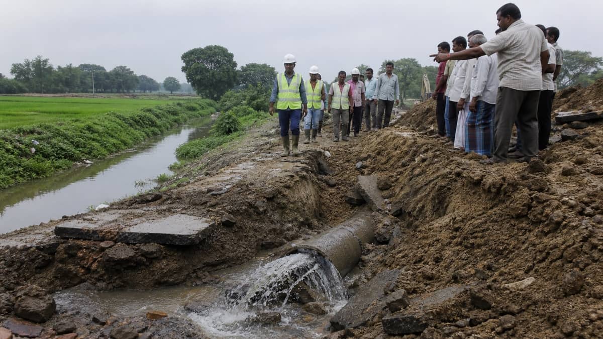 Inspection workers examining a damaged pipeline beside farmland near Dinapur