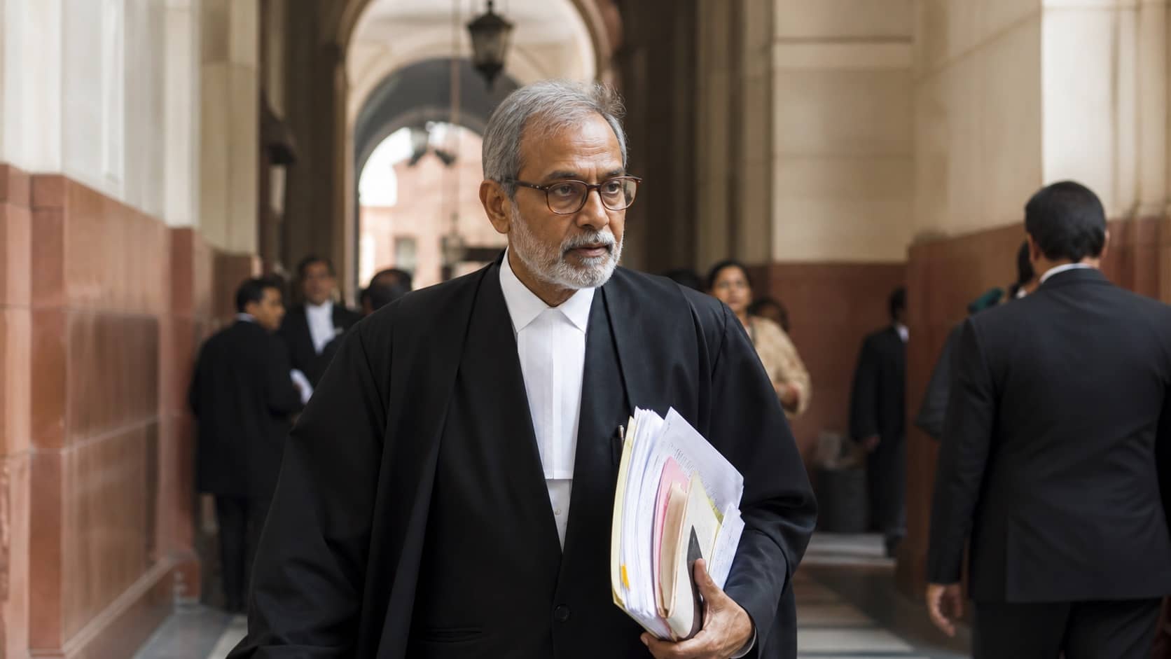 Senior advocate walking through a Supreme Court corridor carrying legal briefs