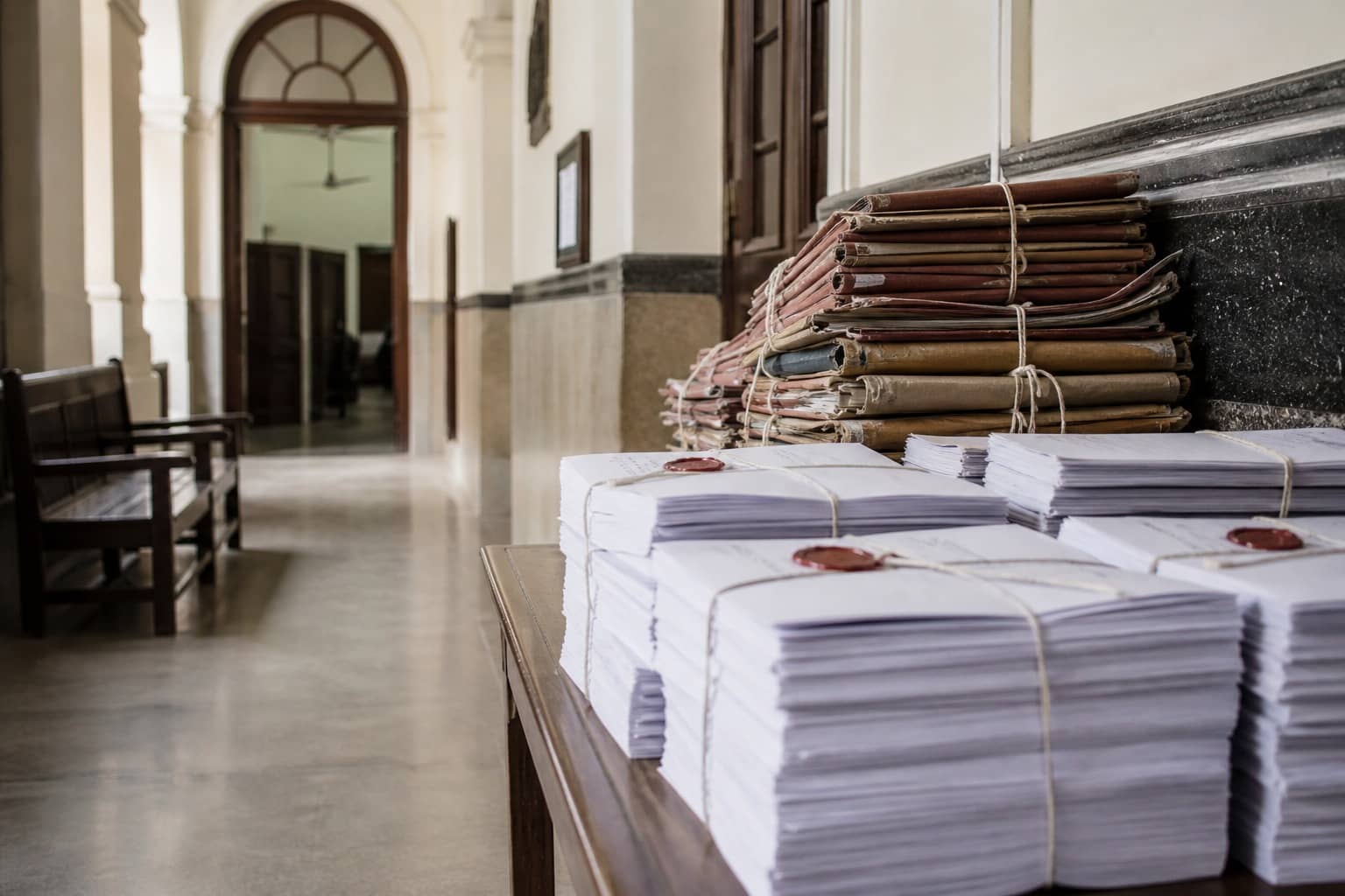 Representational illustration of court papers and exam answer booklets on a wooden table in an Indian institutional setting