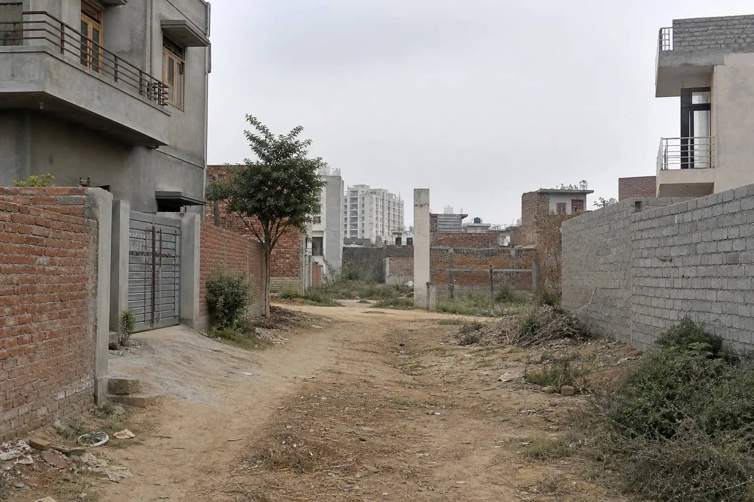 Narrow residential colony lane with unfinished construction boundaries in Gurugram outskirts