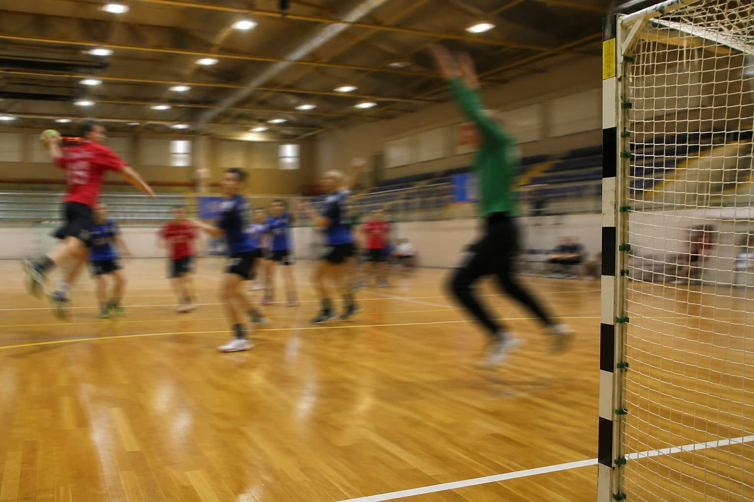 Illustrative indoor handball court with anonymous youth players and a scoreboard graphic