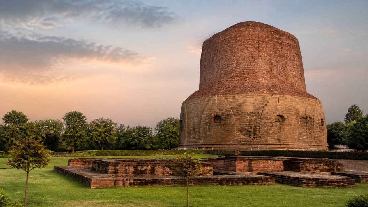 Illustrative photorealistic view of the ancient brick Dhamek Stupa at Sarnath under soft daylight with green lawns and clear sky