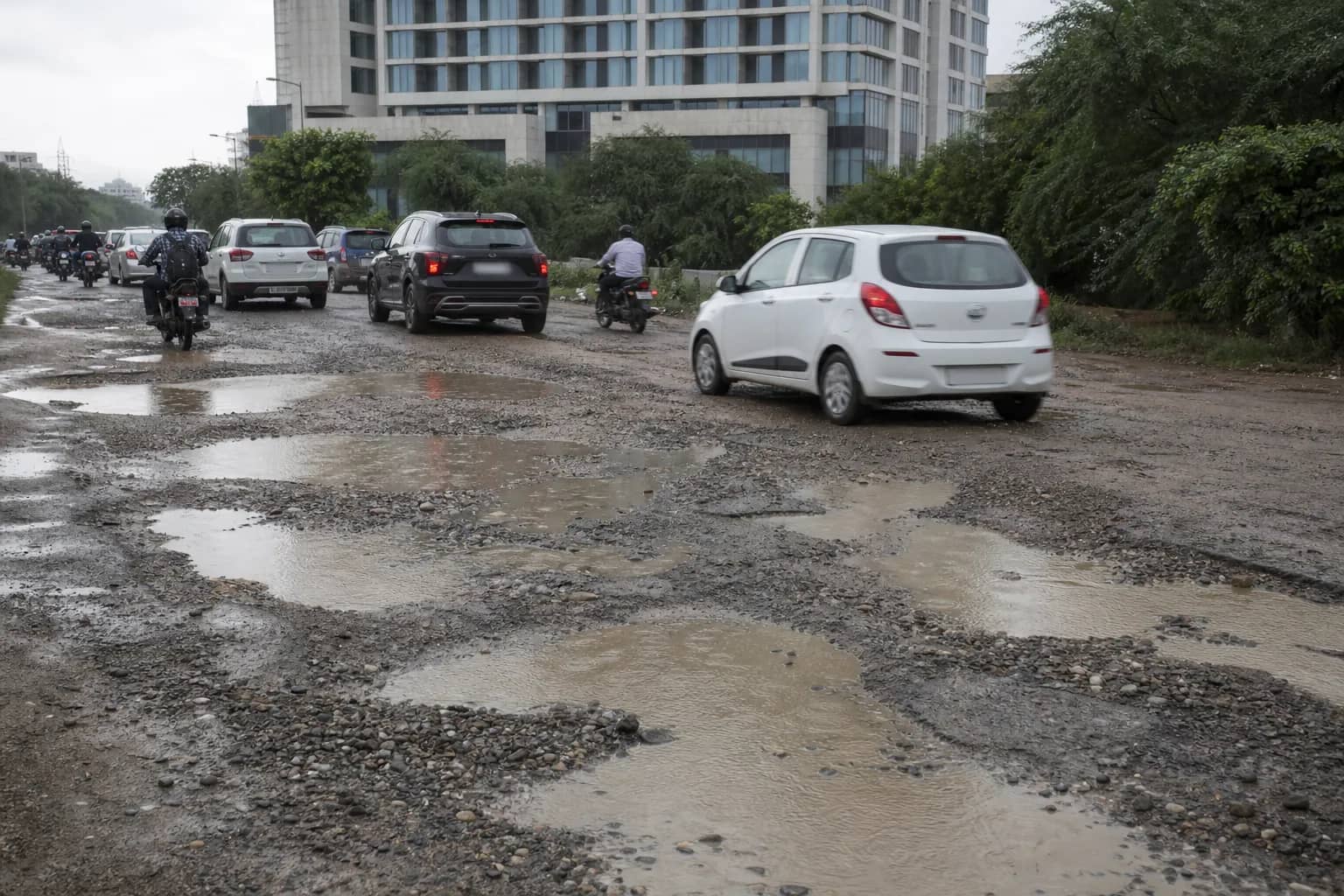Deep potholes and loose gravel on a Gurugram service road