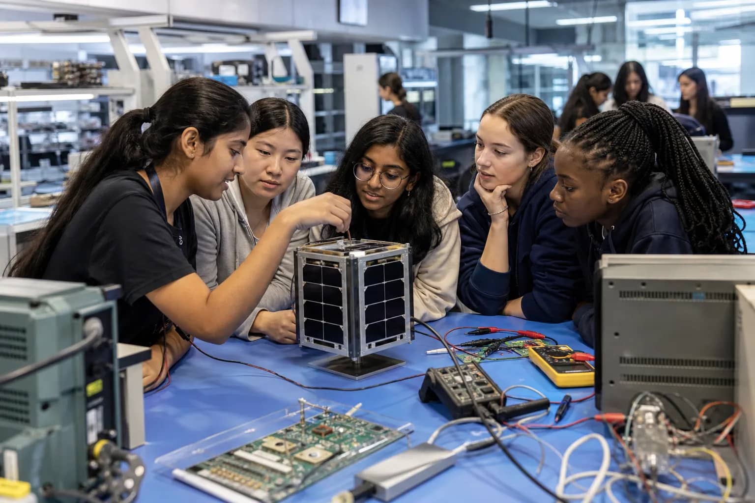 Girl students examining a small satellite model in a university laboratory