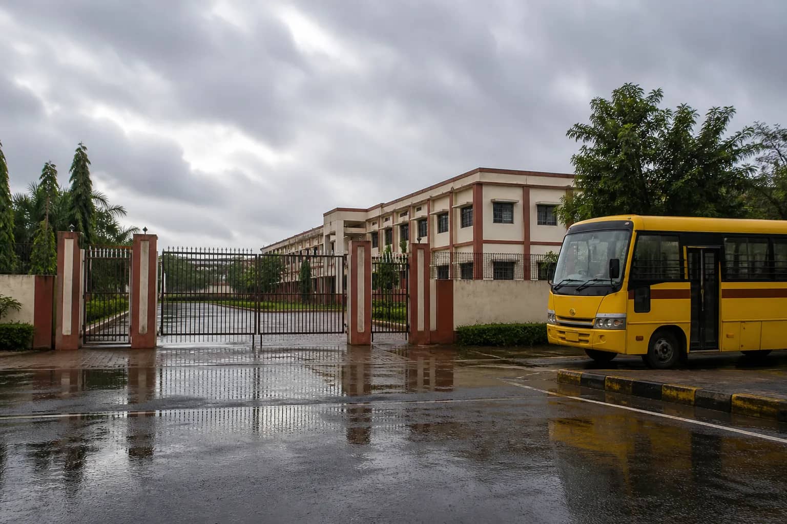 Closed Indian school gate on a rainy overcast morning with an empty school bus nearby