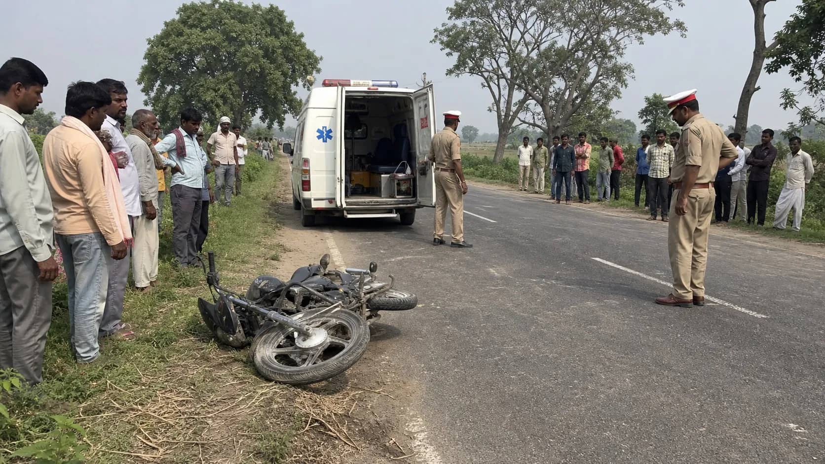 Damaged motorcycle beside a rural road as an ambulance arrives