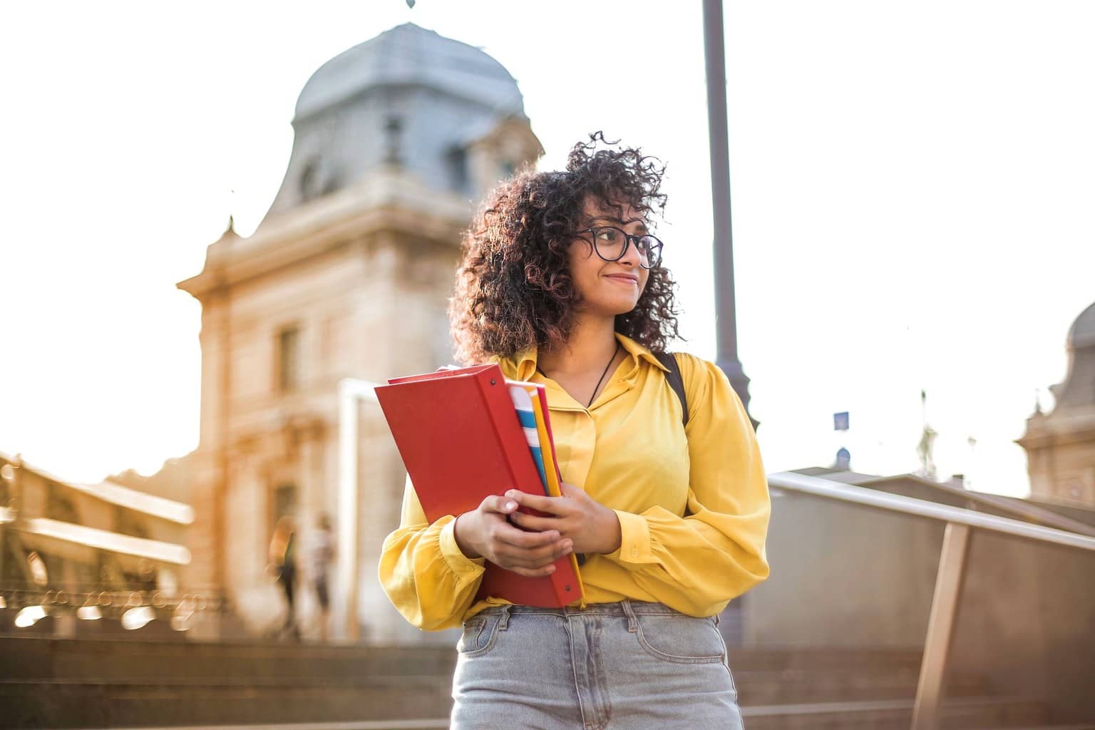 Representational illustration of a student holding admission folders on campus steps