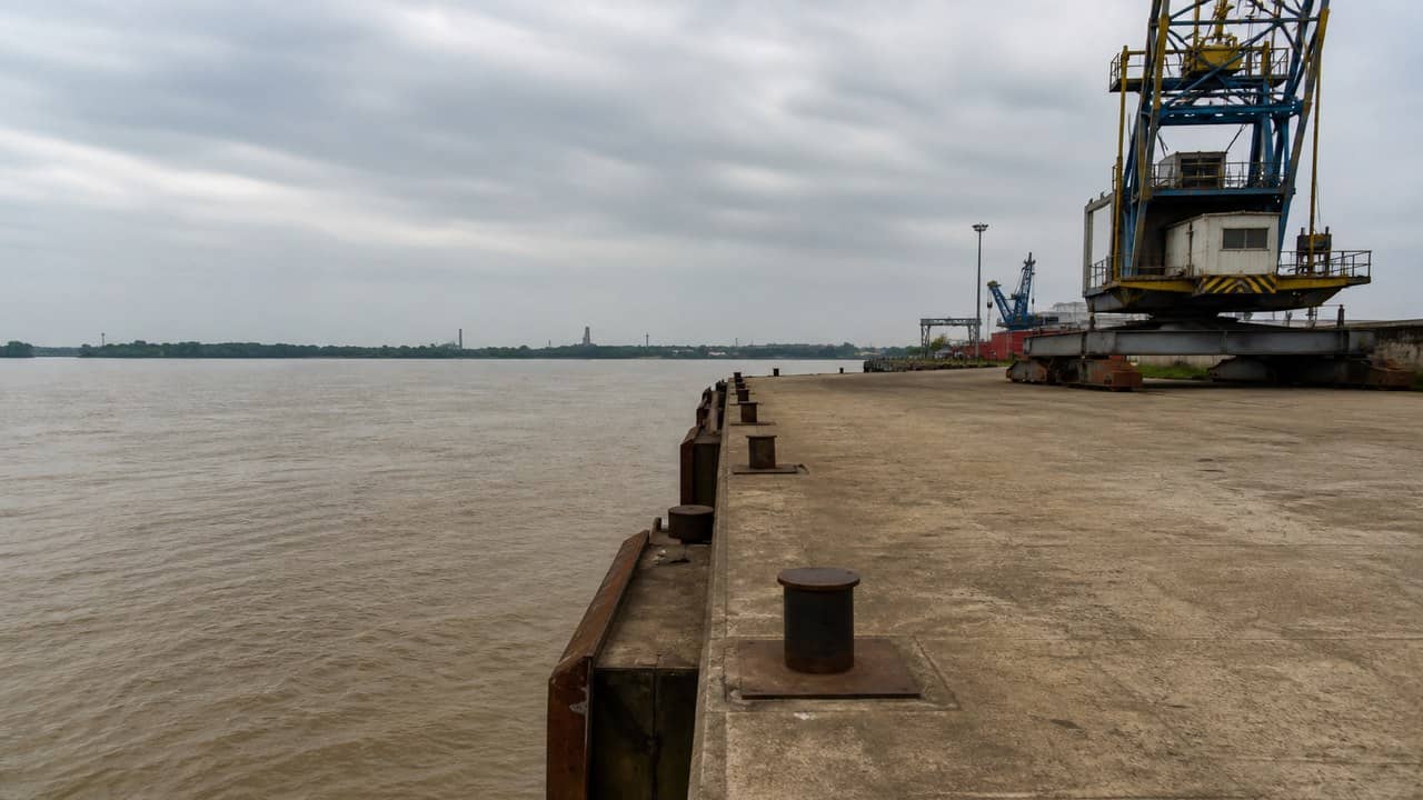 Photorealistic empty inland waterway cargo terminal quay on a wide Indian river, concrete jetty and steel bollards, calm brown water, overcast sky, no people, no logos or readable signs