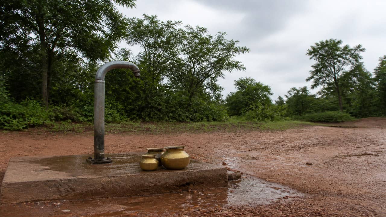 Photorealistic empty rural Indian public standpipe with a metal tap over a wet concrete platform on a dirt path, overcast daylight, no people, no logos or readable signs