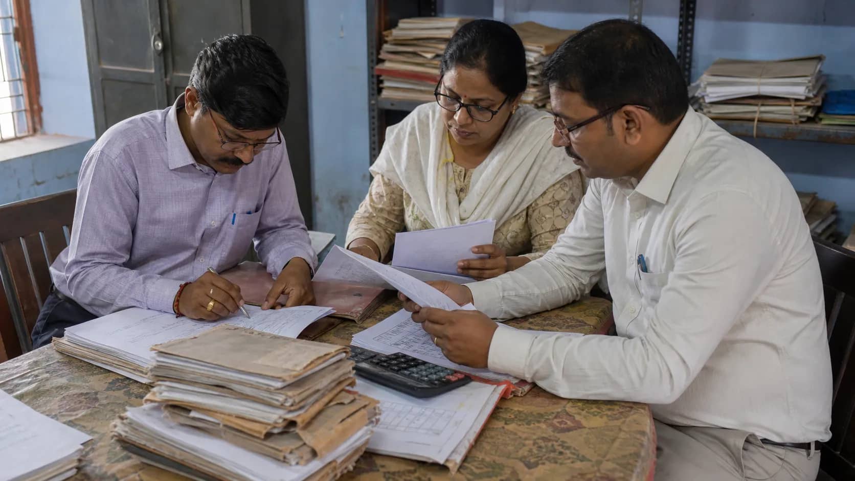 Teachers reviewing old salary files in a Varanasi school office