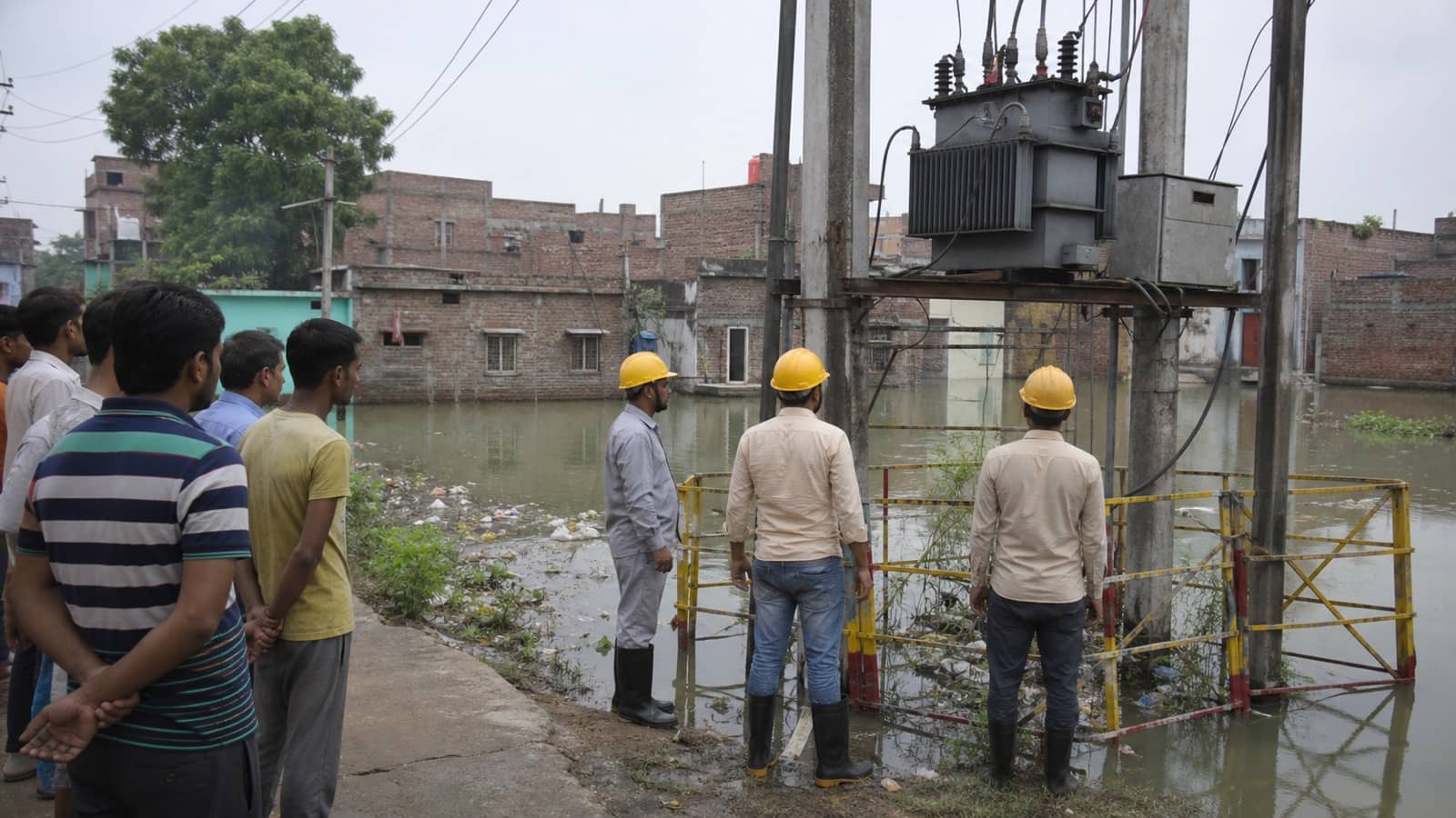 Electricity workers monitoring a distribution box beside floodwater in Salarpur