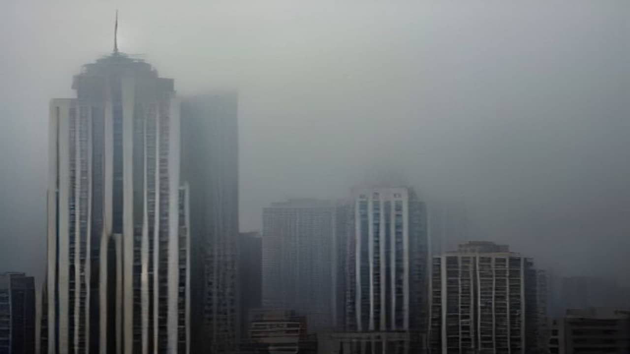 Empty city skyline of mid-rise buildings under a hazy grey monsoon sky, soft atmospheric haze, no people in foreground, no logos or readable signs