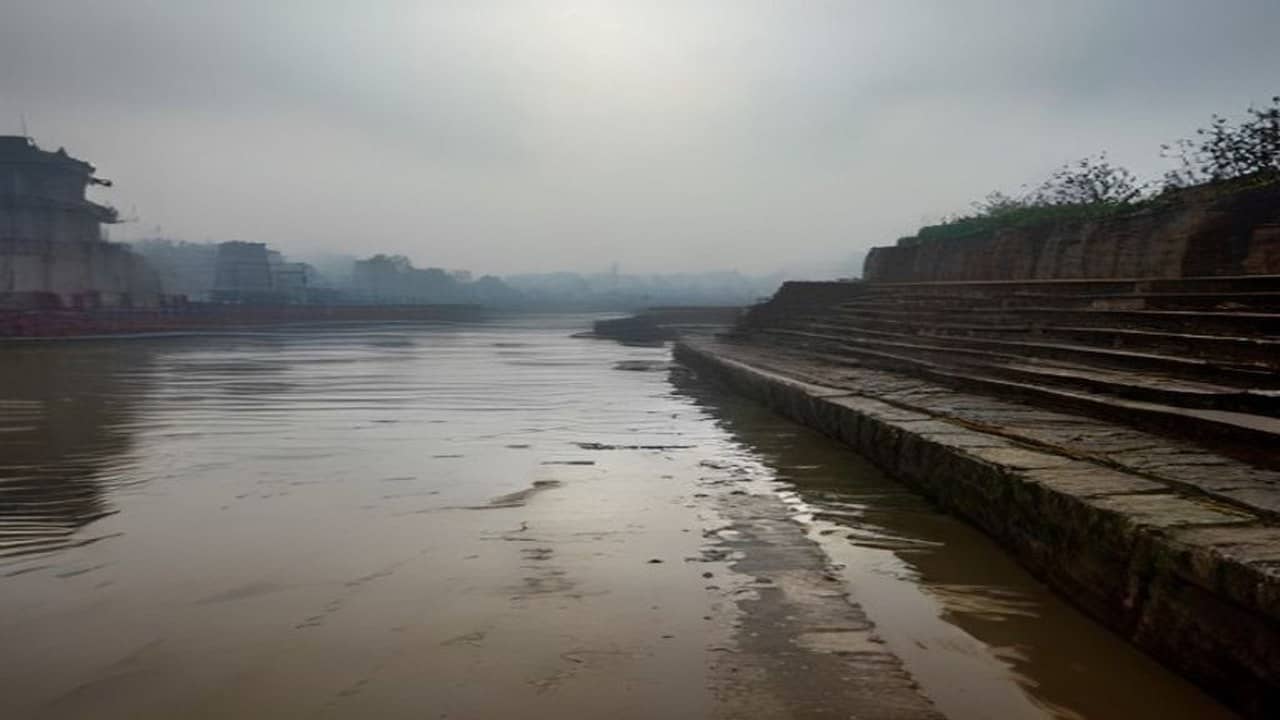 Empty Varanasi ghat stone steps with receding brown Ganga water and a silt line under overcast sky, no people, no boats close, no readable text