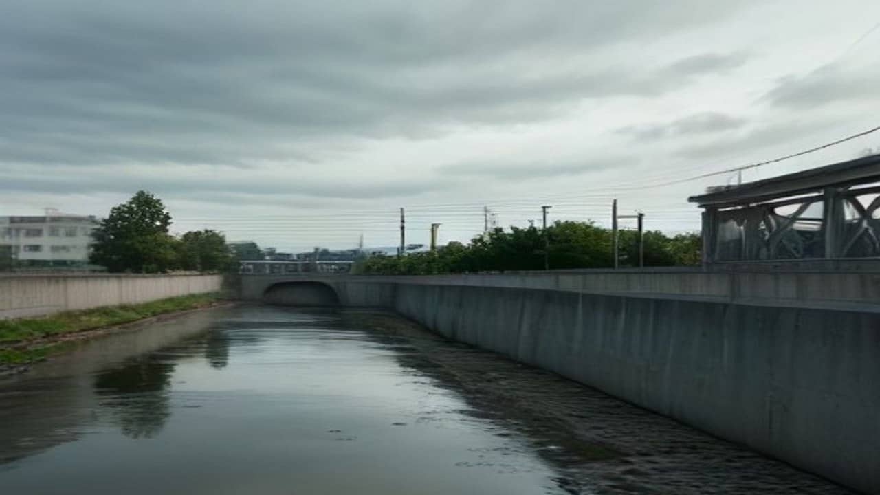 Empty concrete sewage pumping station exterior beside a swollen drain under overcast sky, no people, no logos, no readable text