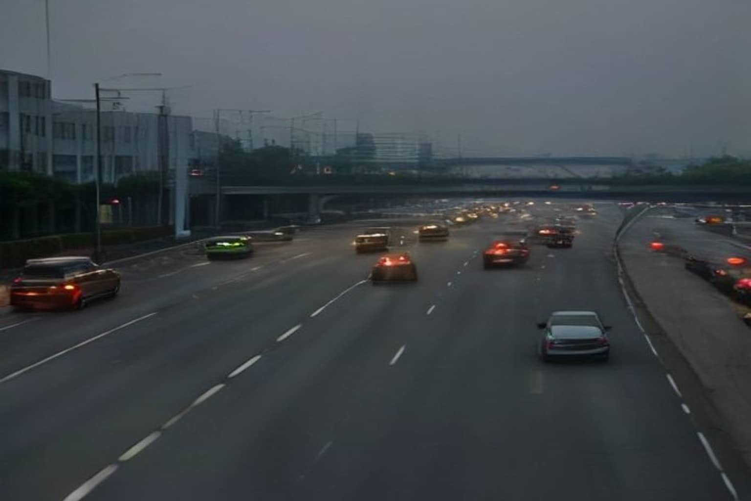 A hazy multi-lane Gurugram expressway with cars showing red taillights under concrete flyover decks, glass buildings faded in grey smog on the left.