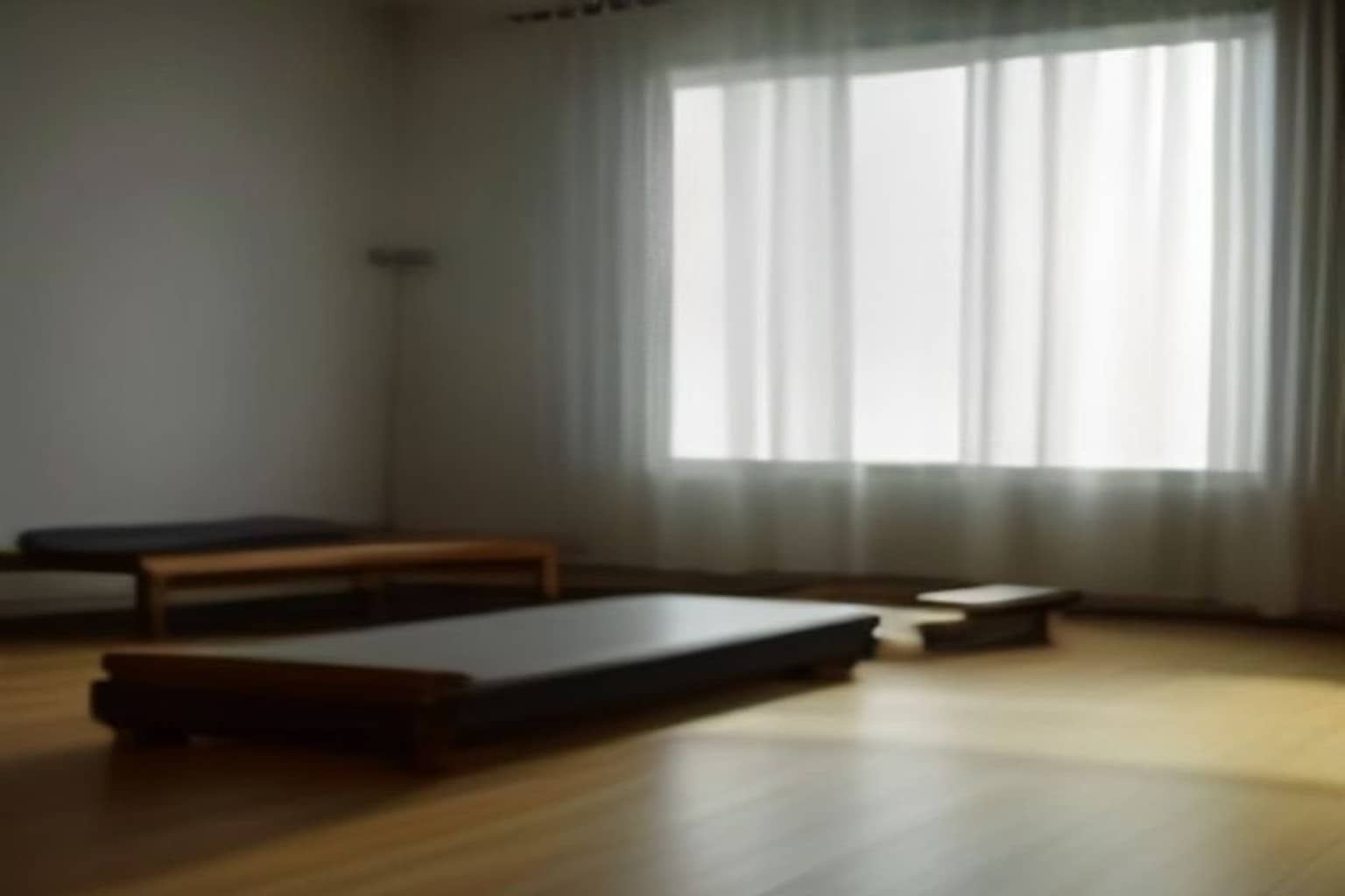 A single Pilates reformer machine with dark padding sits on a light wooden floor in an empty, softly lit studio with white walls.