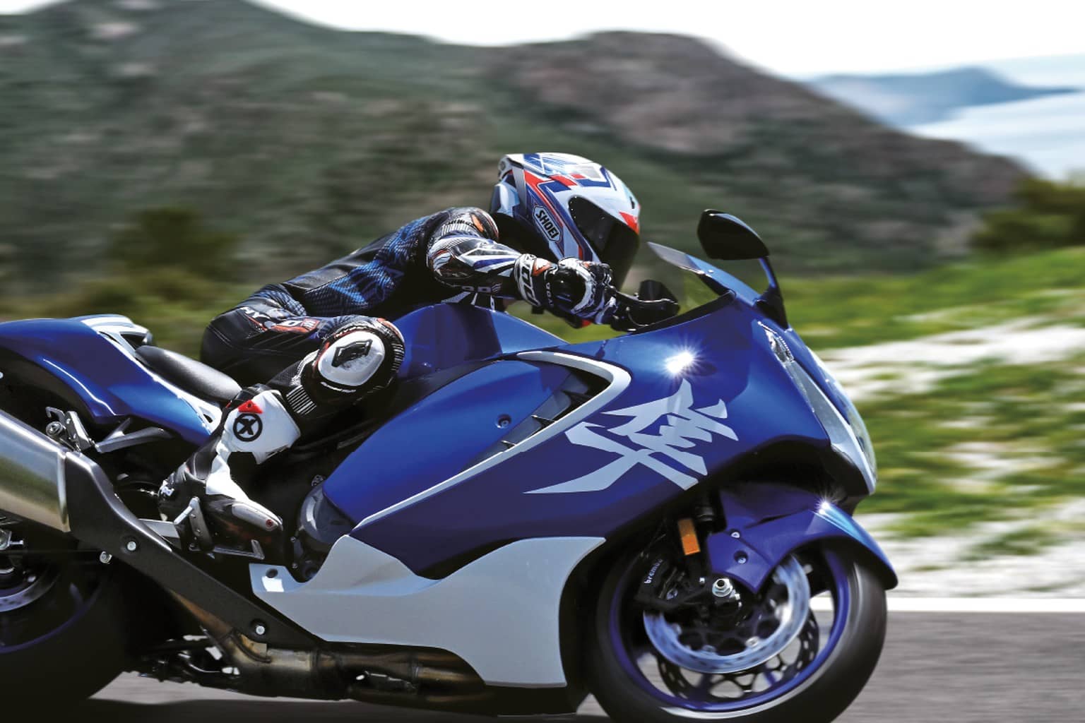 Rider on a blue and white Suzuki Hayabusa sport bike leaning into a coastal mountain road