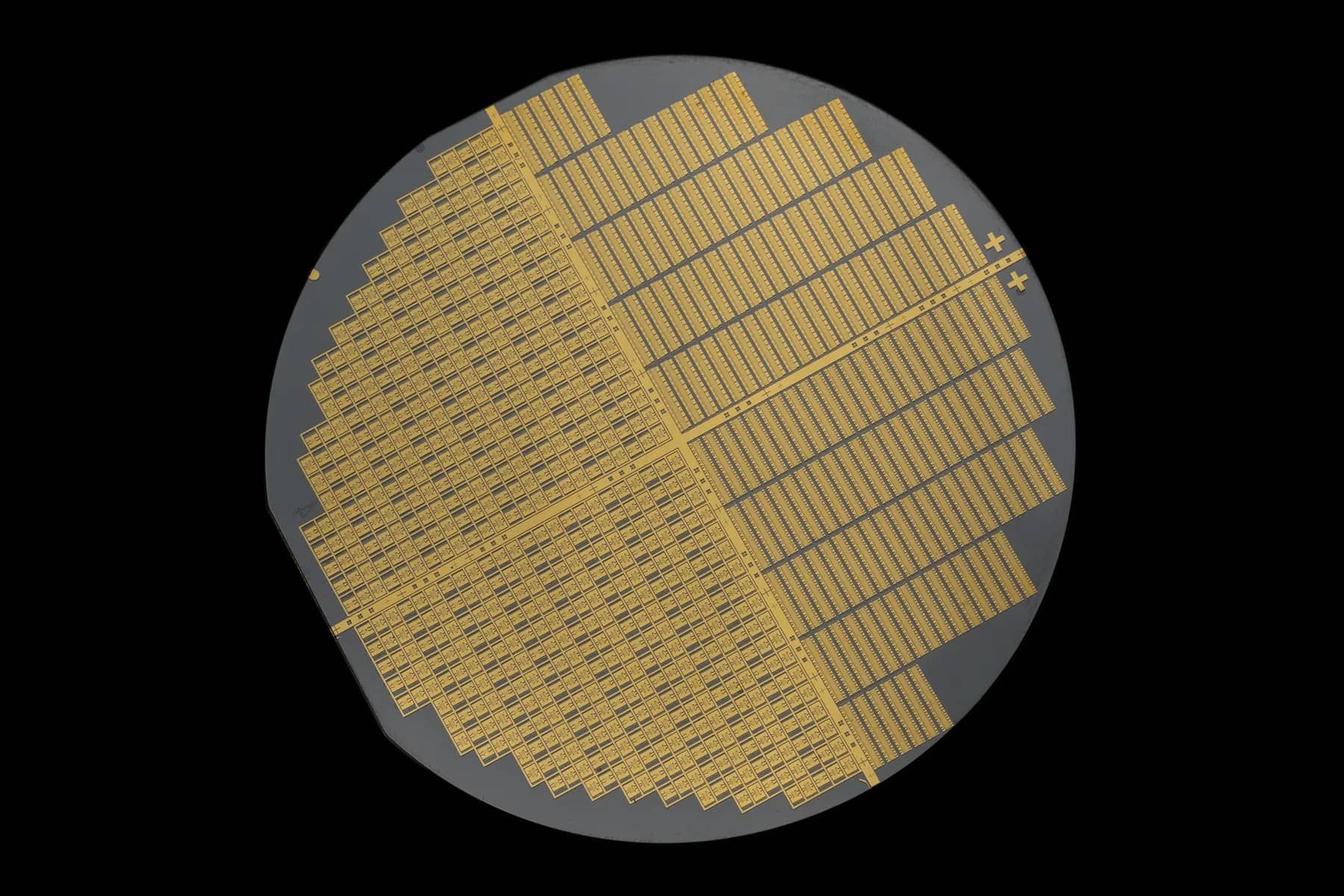 A round gallium nitride semiconductor wafer covered in rows of small gold coloured transistor dies, shown against a black background