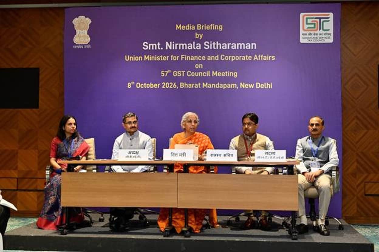 Five officials seated at a table on a stage in front of a purple backdrop announcing a media briefing on the 57th GST Council meeting at Bharat Mandapam, New Delhi
