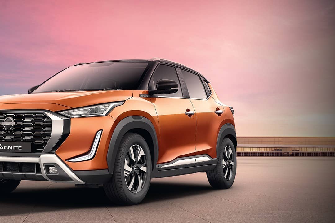 Orange Nissan Magnite compact SUV with black roof, front three-quarter view against a pink evening sky