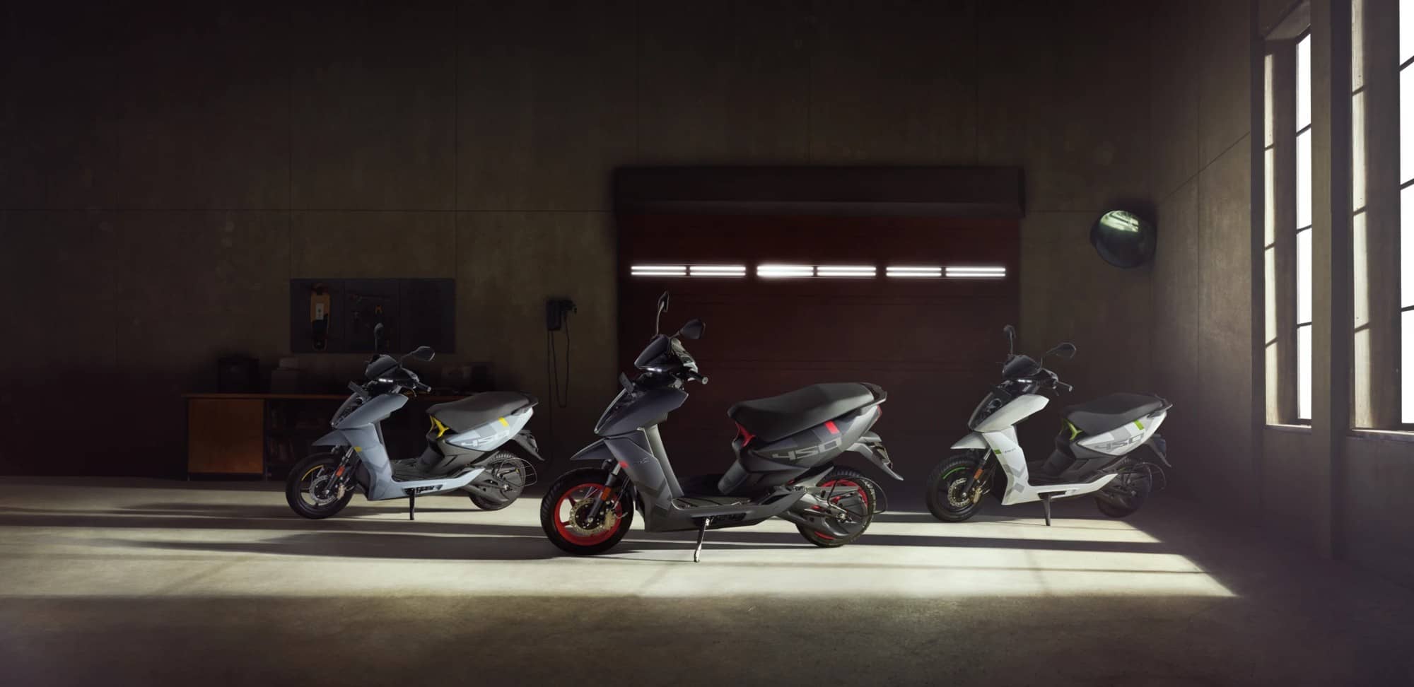 Three Ather 450 electric scooters parked in a dim garage with light from a window