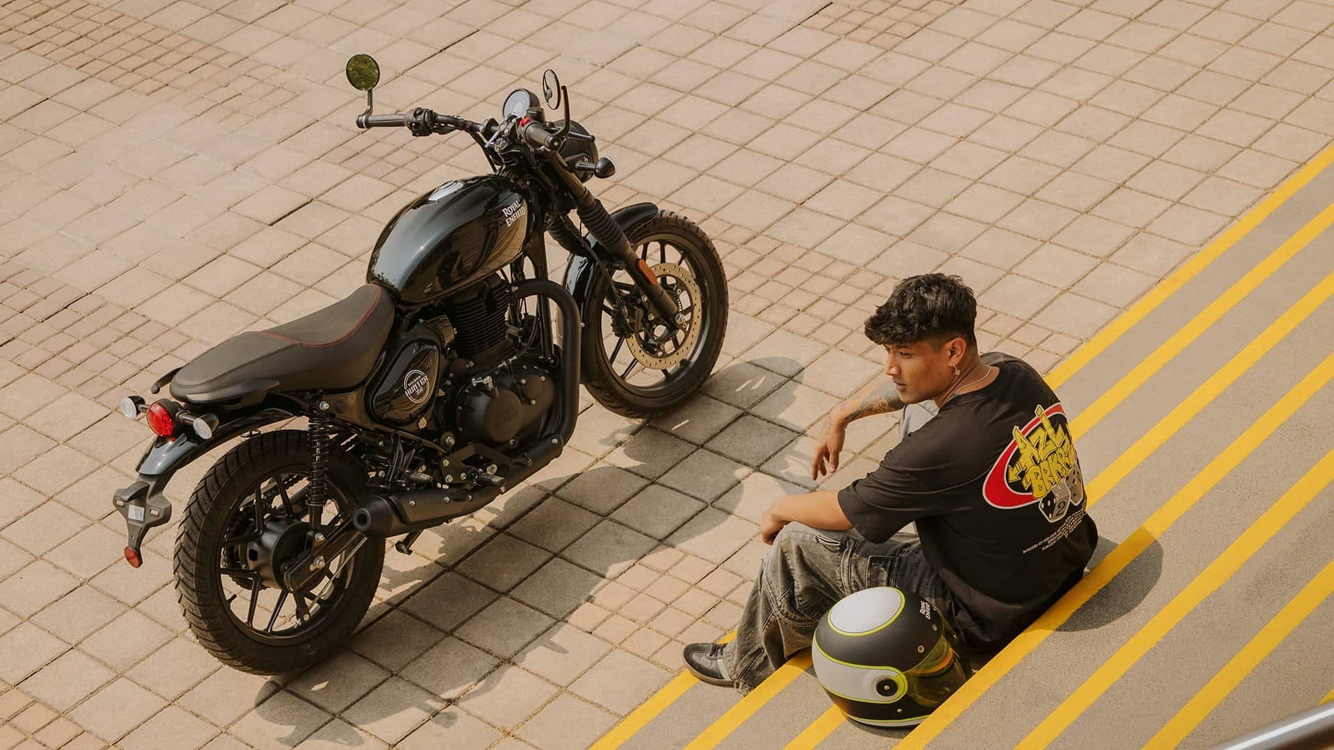 Royal Enfield Hunter 350 parked on a street with a rider sitting on the kerb beside it