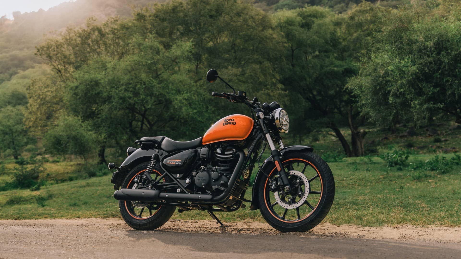 Royal Enfield Meteor 350 in orange and black parked on a road with trees behind