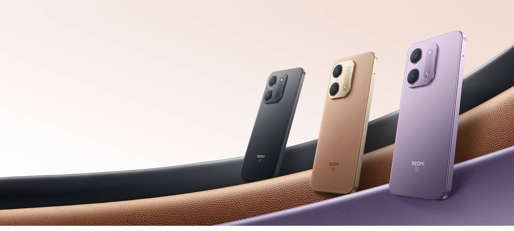 Three Redmi 17C 5G phones seen from the back in black, tan and purple, resting on curved ribbons in matching colours